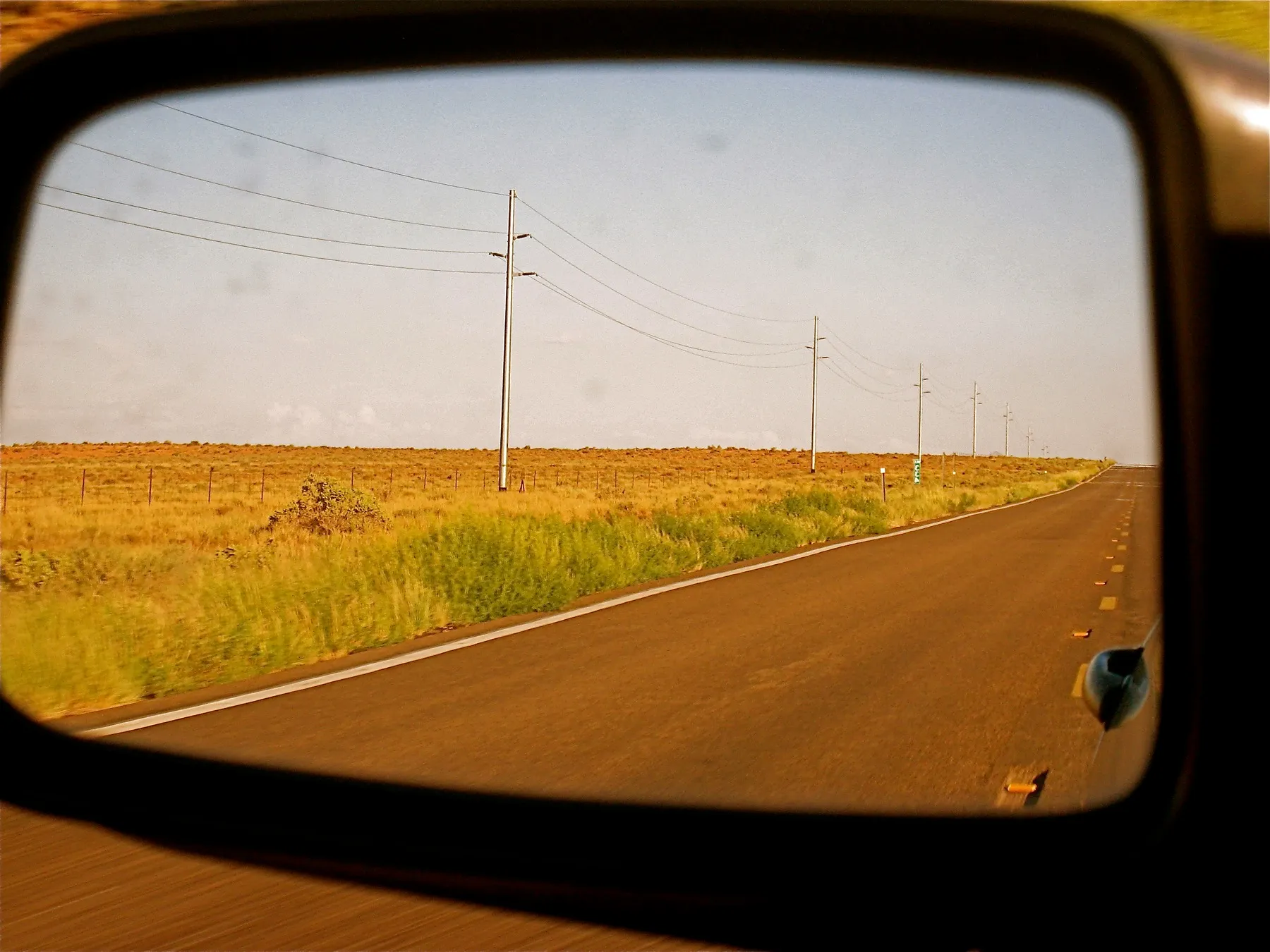 A prairie highway seen in a side mirror